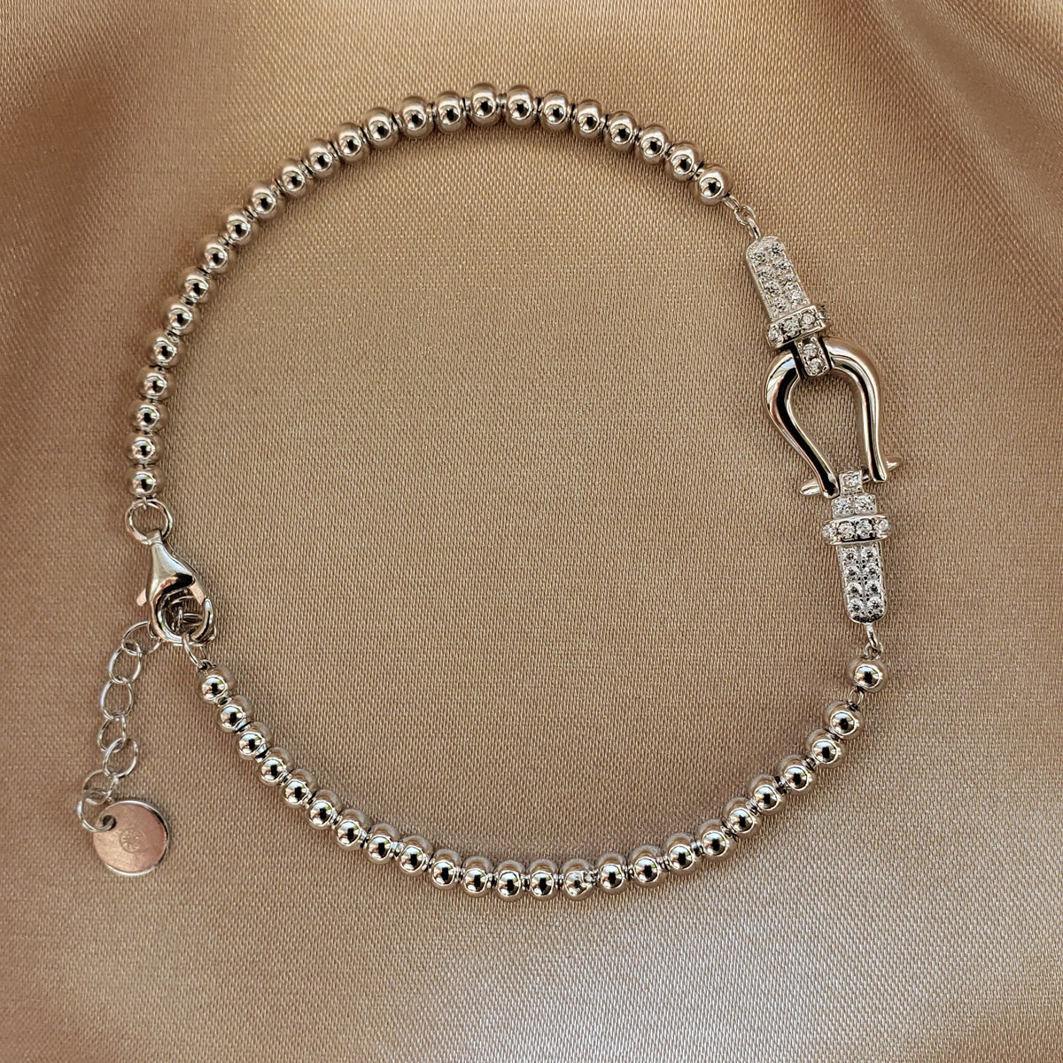 Byzylyk ngjyre argjendi me rruaza te rrumbullaketa dhe motiv ne forme patkoi me gure te bardhe, mbi saten bezhe | Penelope Jewellery