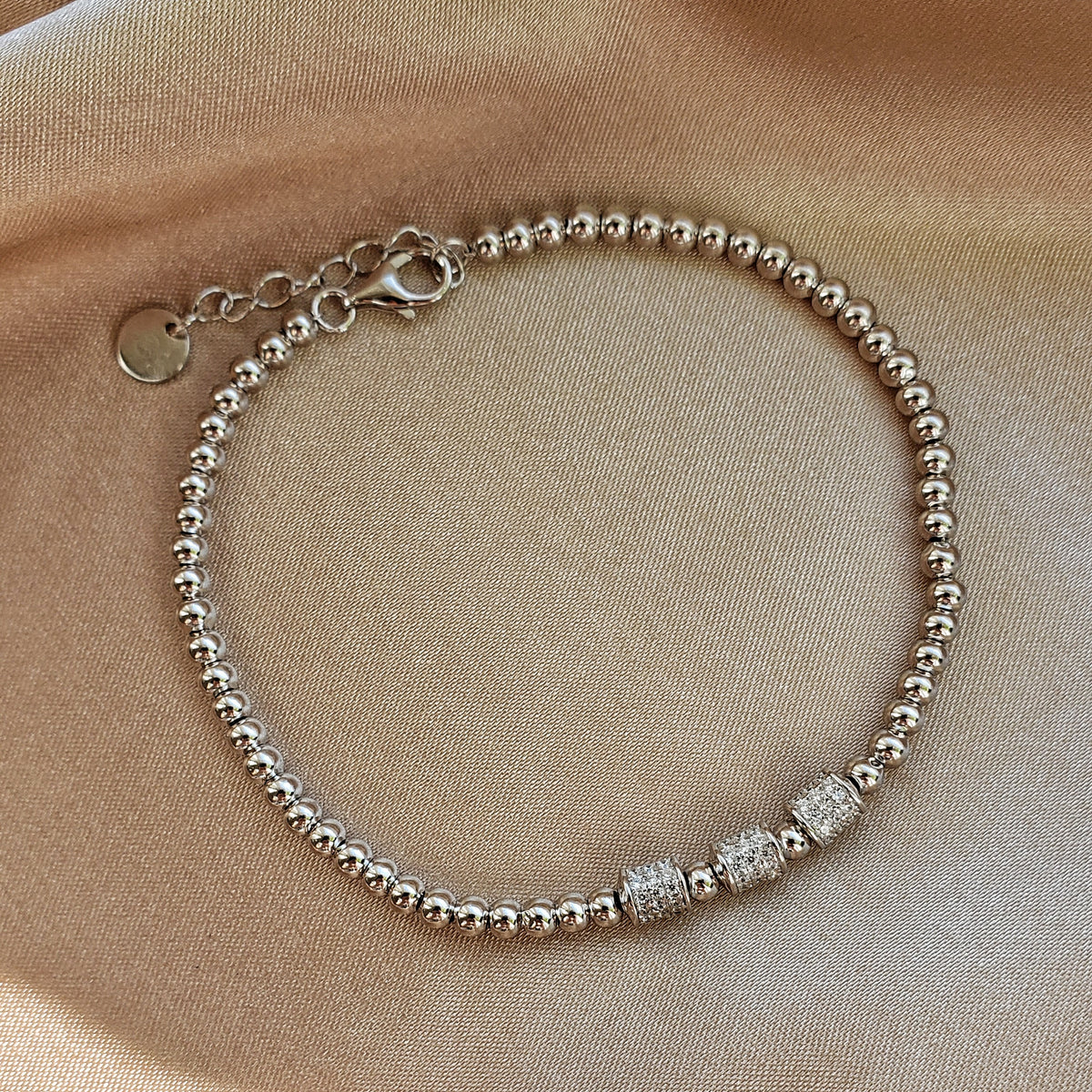 Byzylyk ngjyre argjendi me rruaza te rrumbullaketa dhe tre dekore cilindrike me gure te bardhe, me zinxhir zgjatues mbi saten bezhe | Penelope Jewellery