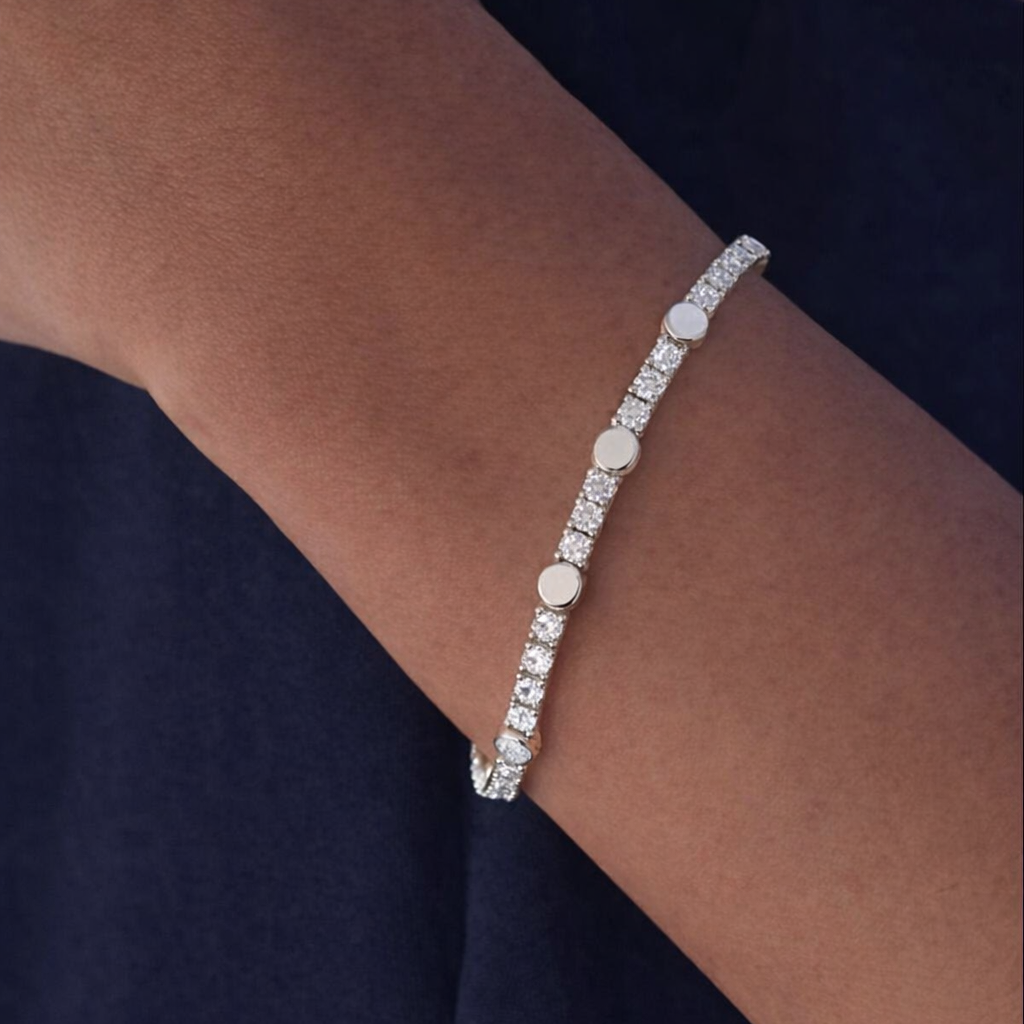 Byzylyk stil tenis ngjyre argjendi me gure te bardhe dhe disqe te rrumbullaketa te lemuara, i veshur ne dore ne sfond te erret | Penelope Jewellery
