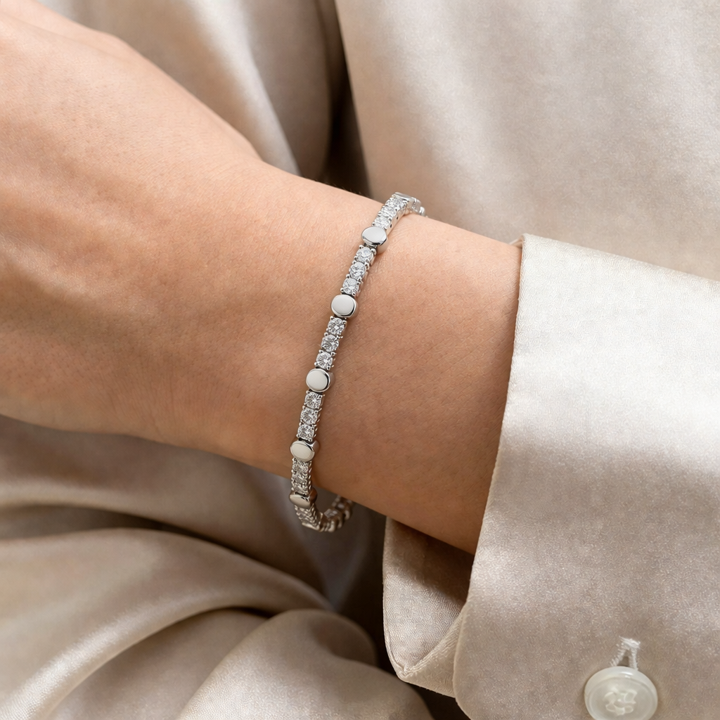 Byzylyk stil tenis ngjyre argjendi me gure te bardhe dhe disqe te rrumbullaketa, i veshur ne dore prane menges ngjyre krem | Penelope Jewellery