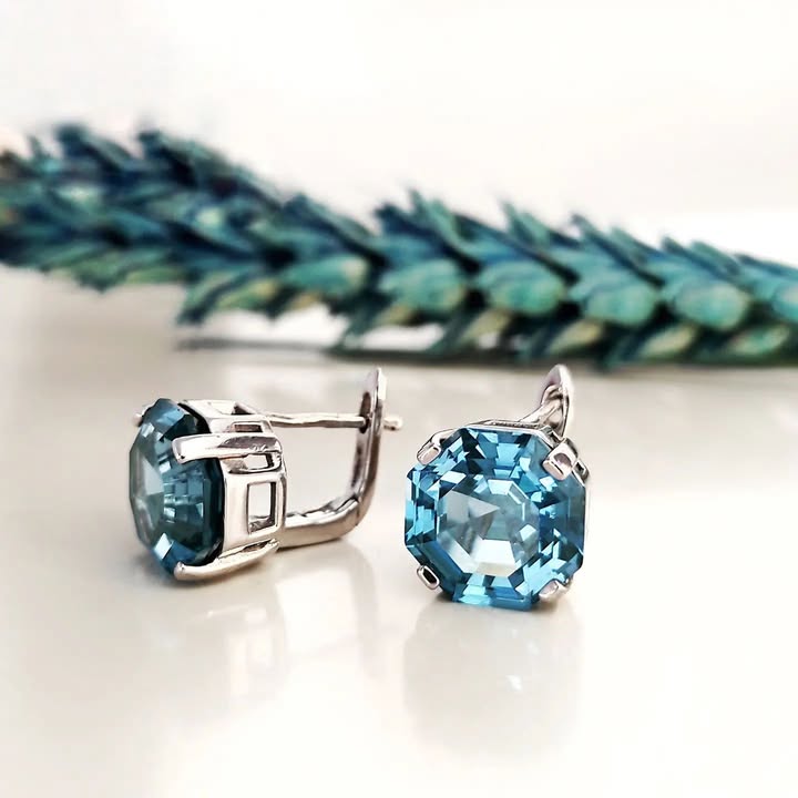 Vathe ngjyre argjendi me gure blu katrore me qoshe te prera dhe kapese te mbyllur, pamje ballore dhe anash me dekor bimor blu ne sfond | Penelope Jewellery