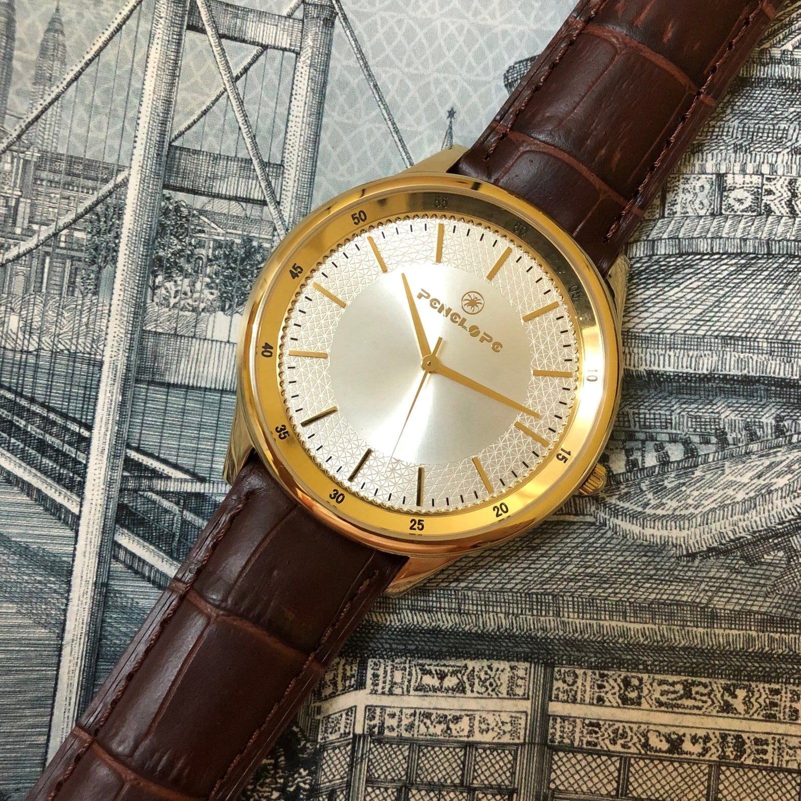 Gold wristwatch with textured silver dial and brown leather strap